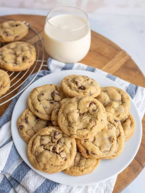 top view of a plate stacked with chocolate chip cookies with milk and some other cookies on a drying rack