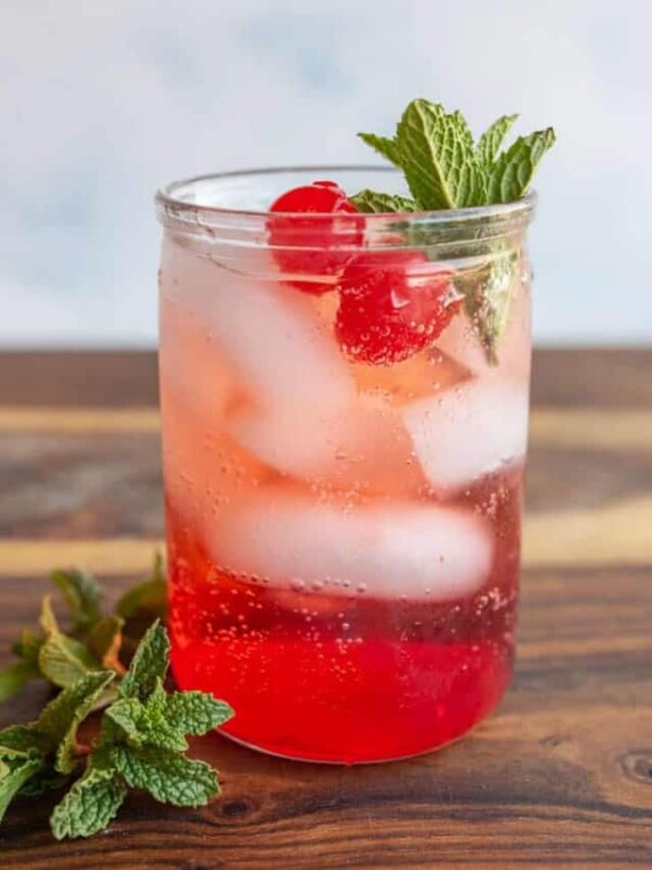 tumbler of a red "Shirley-Temple" drink with ice cherries and garnish