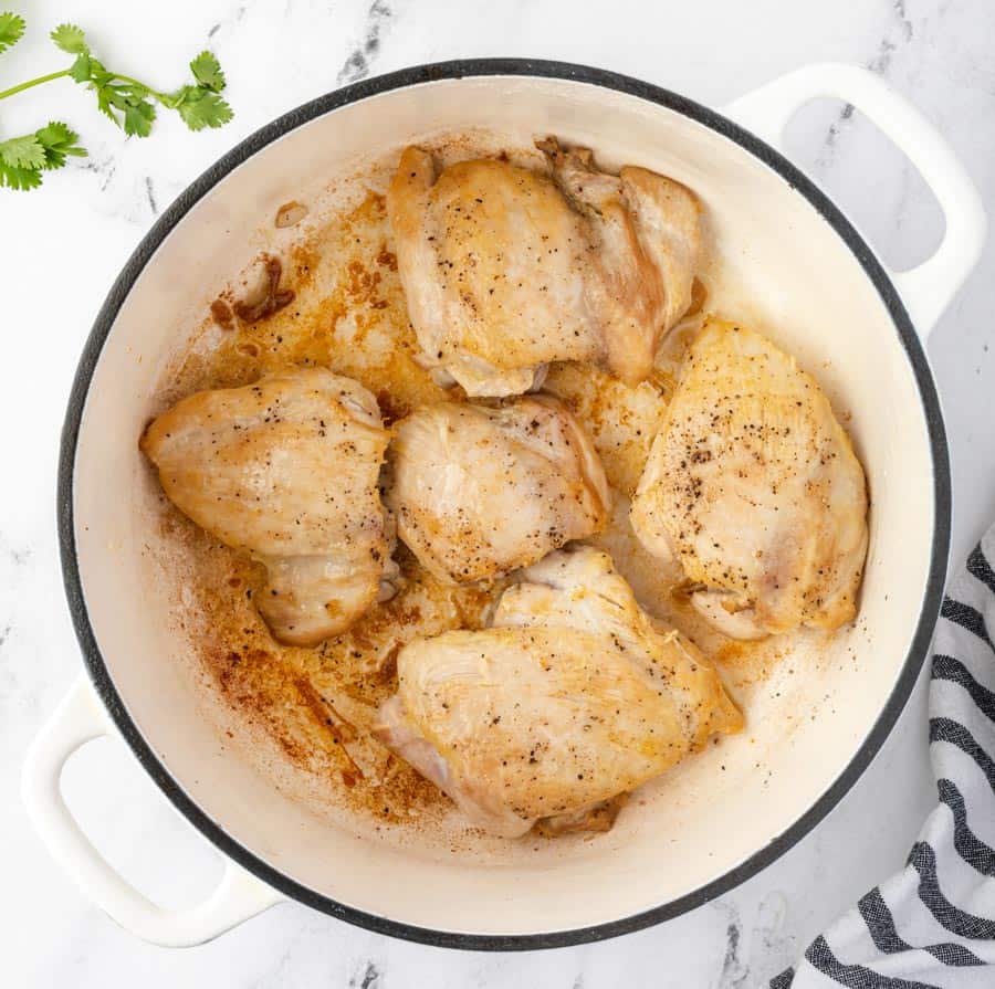 top view of cast iron pot with seasoned chicken in a coconut sauce and spices