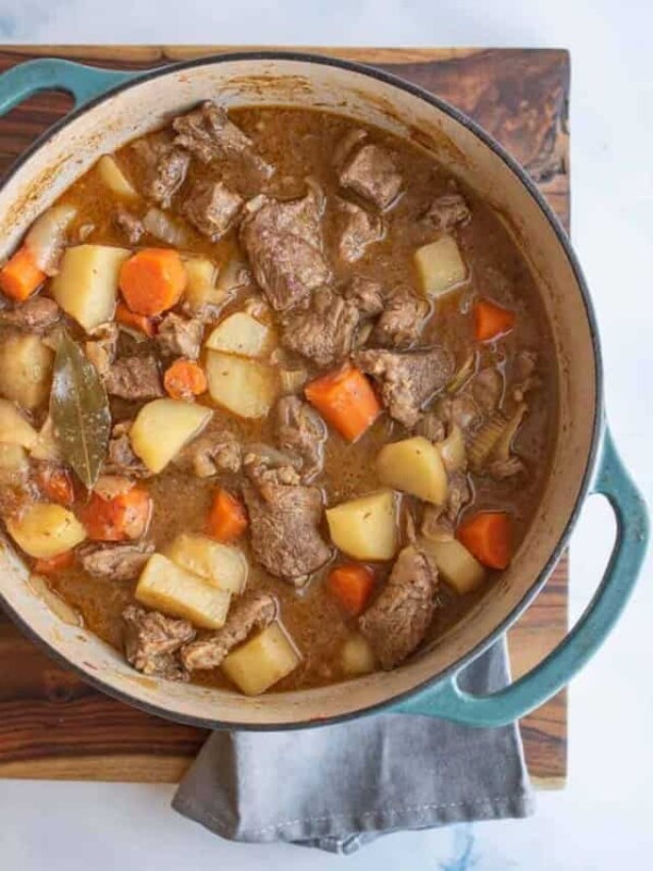 blue dutch oven with beef stew in it, looking from the top down, sitting on a cutting board