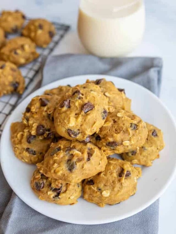 stacked breakfast cookies on a white plate with some on a cooling rack and a glass of milk in the background