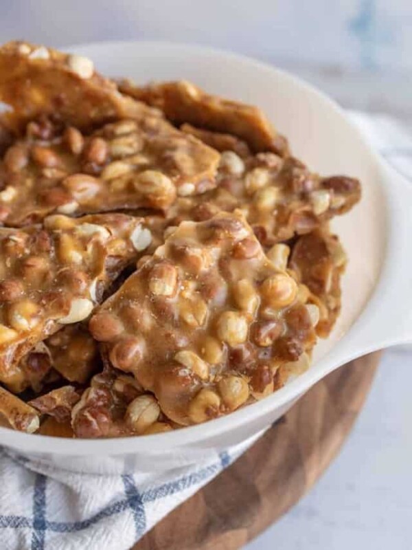 a close up of a white bowl with shards of homemade peanut brittle