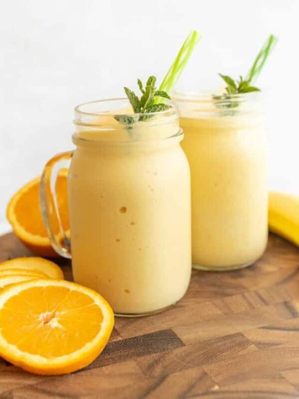 side view of two tropical yellow smoothies in mason jars with a handle