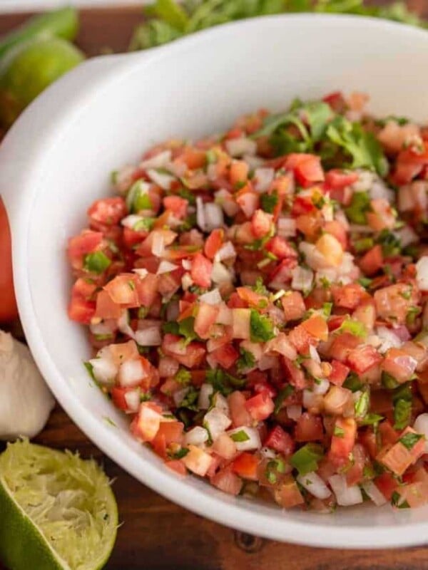 a white bowl with chunky cut tomatoes, onion, herbs in a fresh pico de gallo surrounded by limes