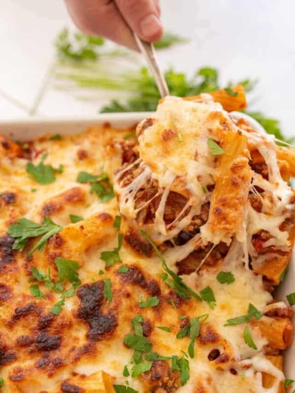 spoon pulling out ingredients from a baking dish with cheese and rigatoni pasta