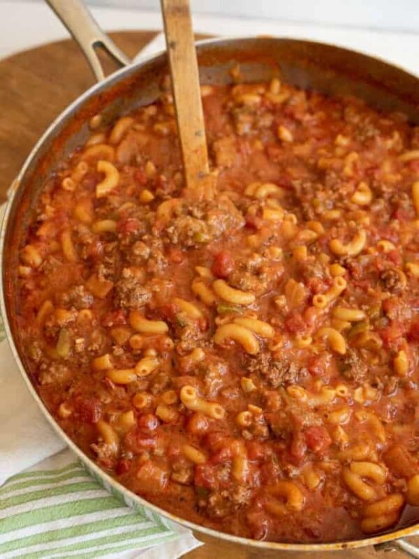 a pot of goulash which is red sauce and elbow pasta like soup with ground beef and a wooden spoon