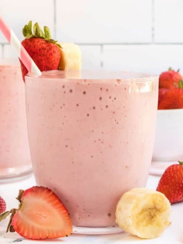 strawberry banana smoothies in cups with pink striped paper straws and fresh fruit all around