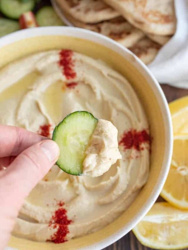 bowl of hummus with red spice on top POV scooping with slice of cucumber