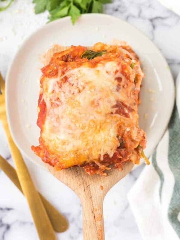 wooden spoon with a square of lasagna POV over a white plate