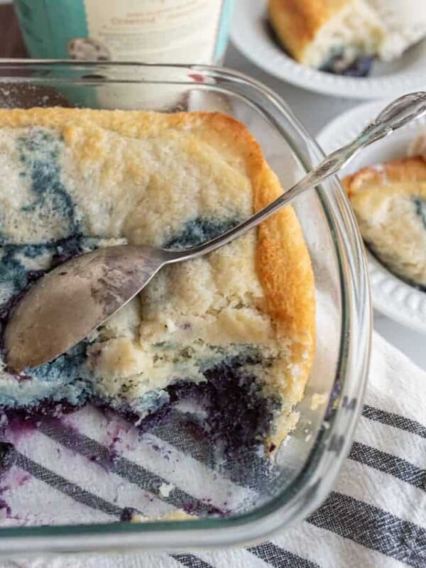 easy blueberry cobbler portioned onto plates with ice cream next to the clear baking dish