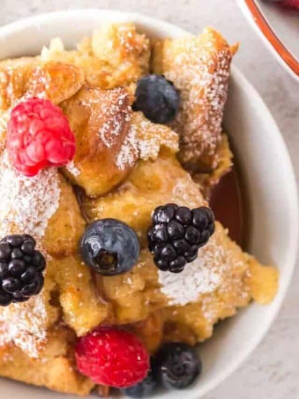 top view of french toast bake with a serving dished onto a plate with powdered sugar berries and syrup