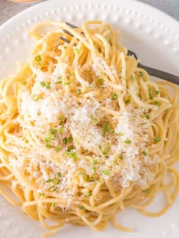 white plate of garlic noodle dinner with cheese and herbs on top