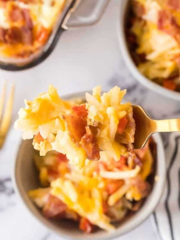 fork full of casserole above small portion dishes of the baked hash brown breakfast casserole with melted cheese and bacon on top