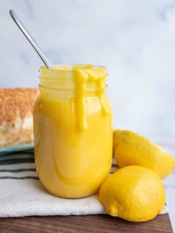 bright yellow lemon curd in a mason jar next to fresh lemons