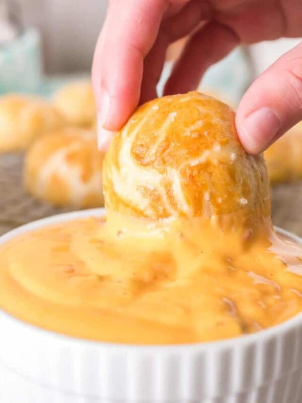 POV hand dipping a pretzel bite into a small dish of cheese sauce