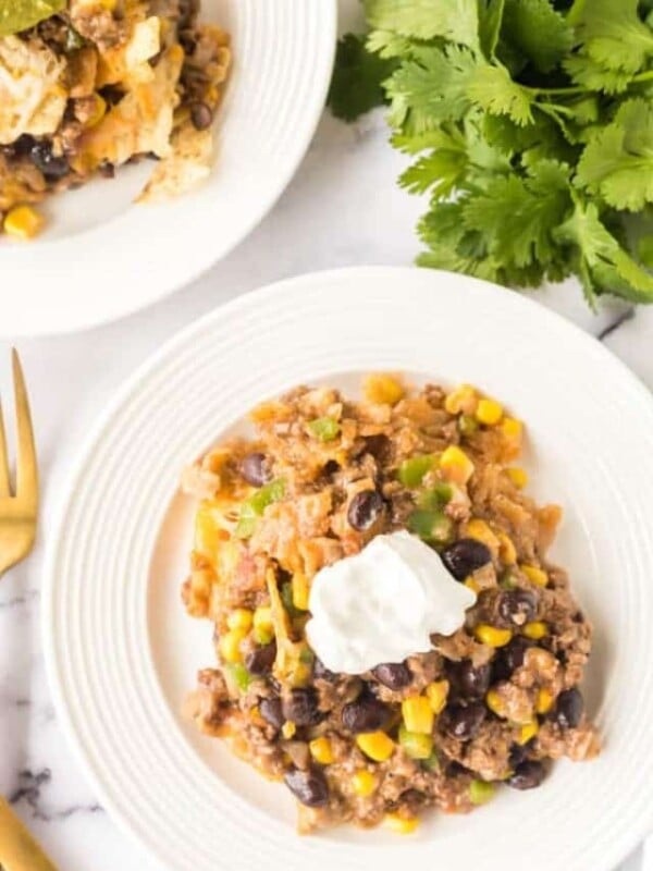 two white plate os taco casserole with sour cream on top.