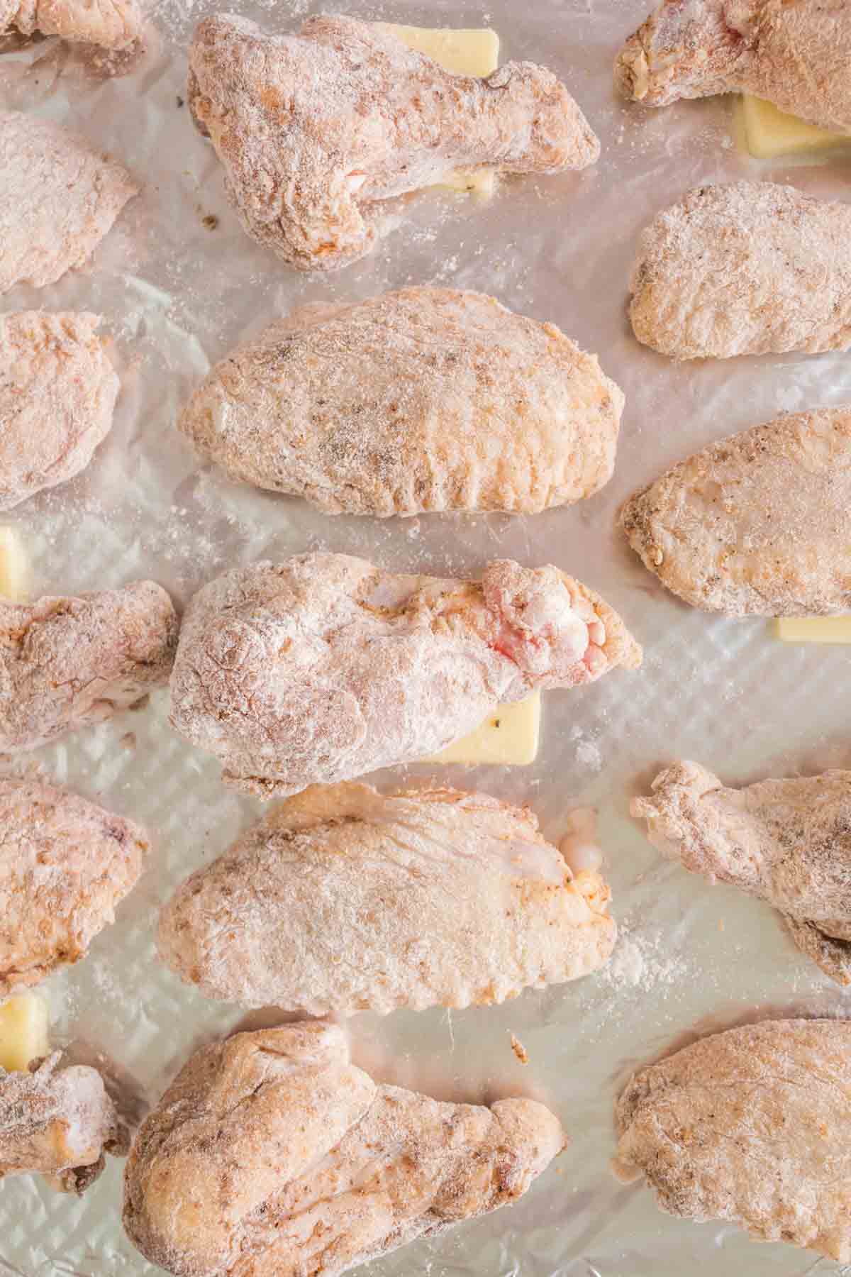 Frozen chicken wings, destined to become fiery hot wings, are evenly arranged on a sheet and glisten with a light layer of frost. They rest in rows on wax paper, ready for transformation.