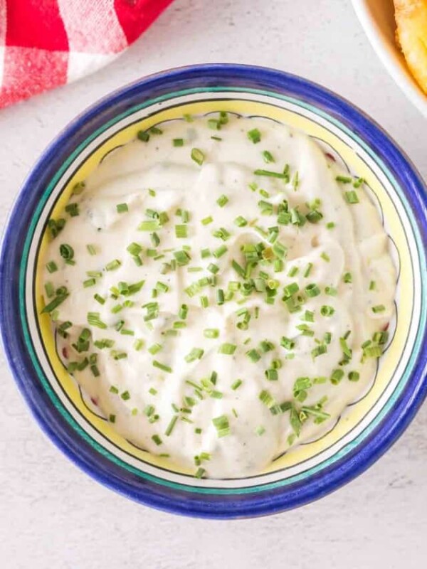 POV dipping fries into a small bowl of aioli with chives on top