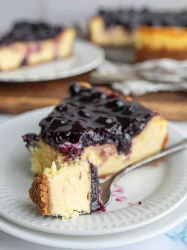 one slice portioned from a whole blueberry cheesecake and a fork full of a bite ready to eat