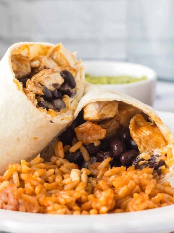 chicken burritos sliced in half with black beans with rice on a white plate