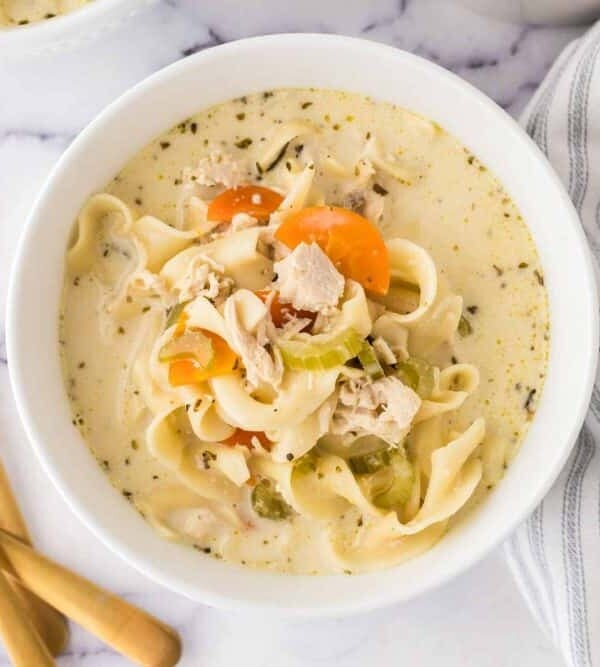 top view of a white bowl of creamy chicken noodle soup and a golden spoon