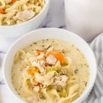 top view of a white bowl of creamy chicken noodle soup and a golden spoon