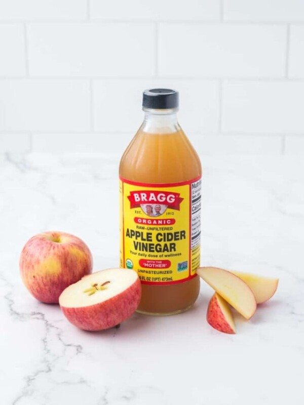 glass bottle of BRAGG organic apple cider vinegar and sliced apples