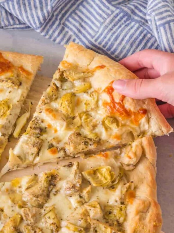 POV hand holding a slice of artichoke pizza