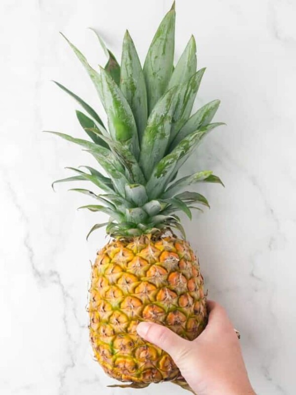 POV hand holding whole pineapple