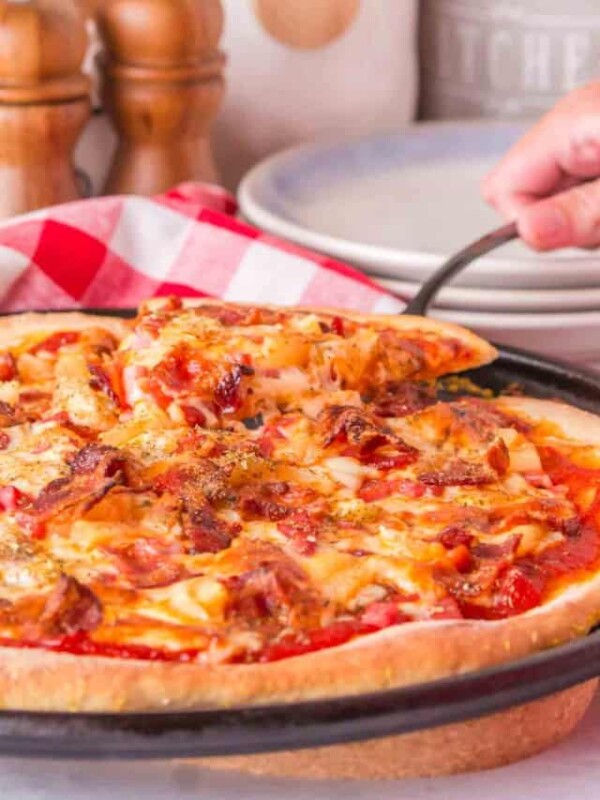 POV hand with spatula pulling a cut slice of pineapple pizza from the pan