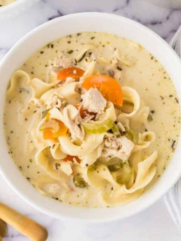 top view of a white bowl of creamy chicken noodle soup and a golden spoon