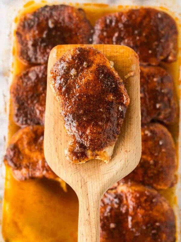 a wooden spatula over a clear baking dish with seasoned pork chops in a sauce