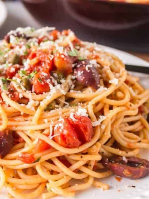 close up of a pasta puttanesca with red sauce on a white plate