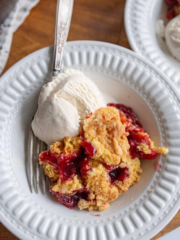 cherry dump cake on a plate with red filling peaking through a crumbly baked crust and ice cream
