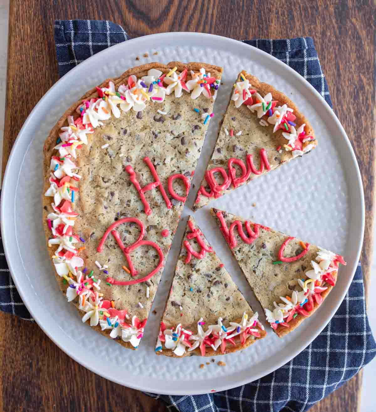 large round chocolate chip cookie cake with birthday decorations sliced.