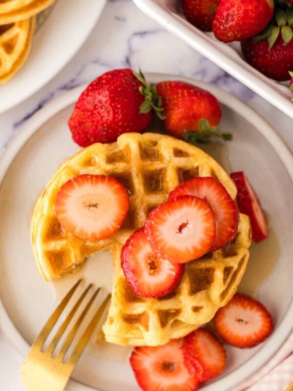 top view of a stack of waffles syrup and fresh strawberries with a slice taken out featuring easy waffle recipes.