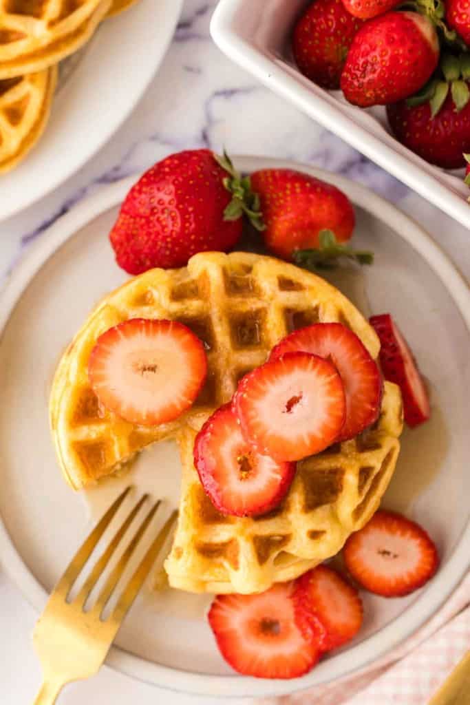 top view of a stack of waffles syrup and fresh strawberries with a slice taken out featuring easy waffle recipes.