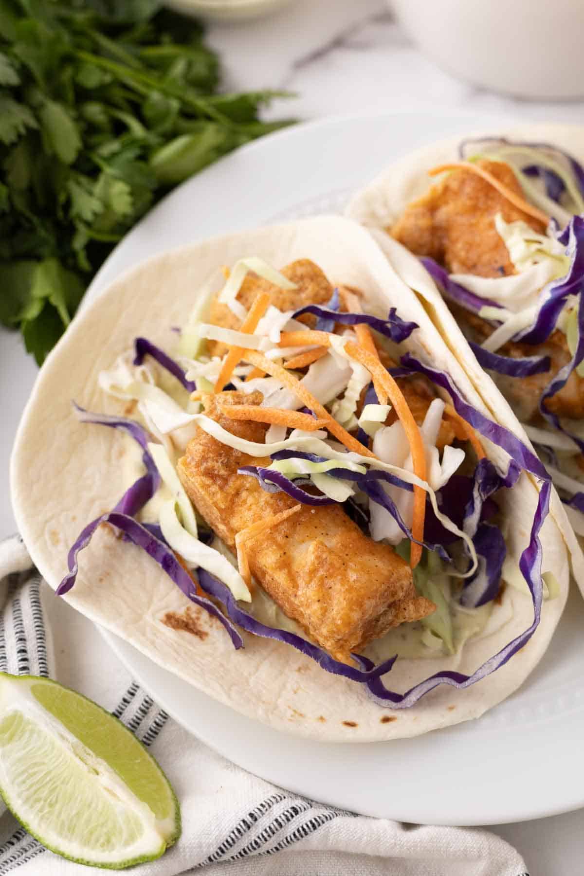 deep fried baja fish taco recipe with cabbage on a flour tortilla with limes.