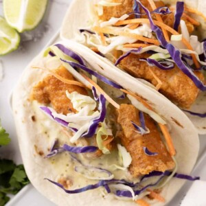 deep fried baja fish taco recipe with cabbage on a flour tortilla with limes.