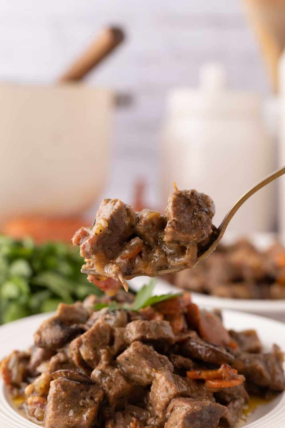 beef Bourguignon recipe served on a white plate with a bite on a golden fork.