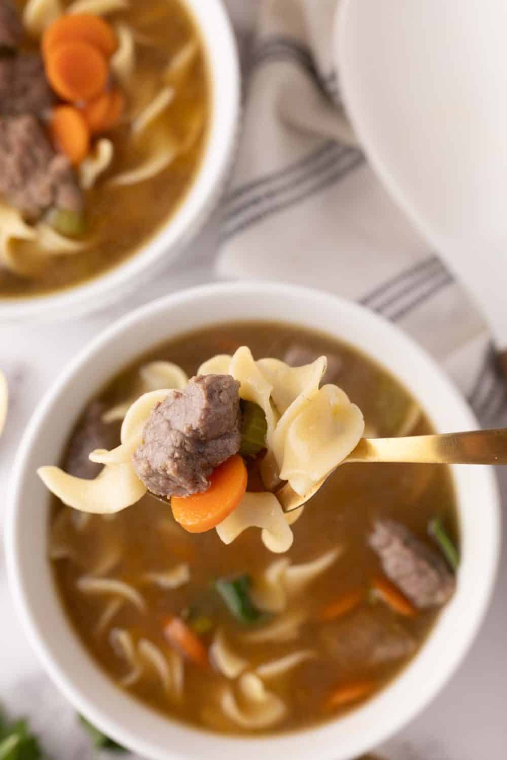 beef noodle soup recipe served in white bowls with golden spoons to the side.