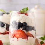 small glass with layered parfait of berries and cream with mint on top.