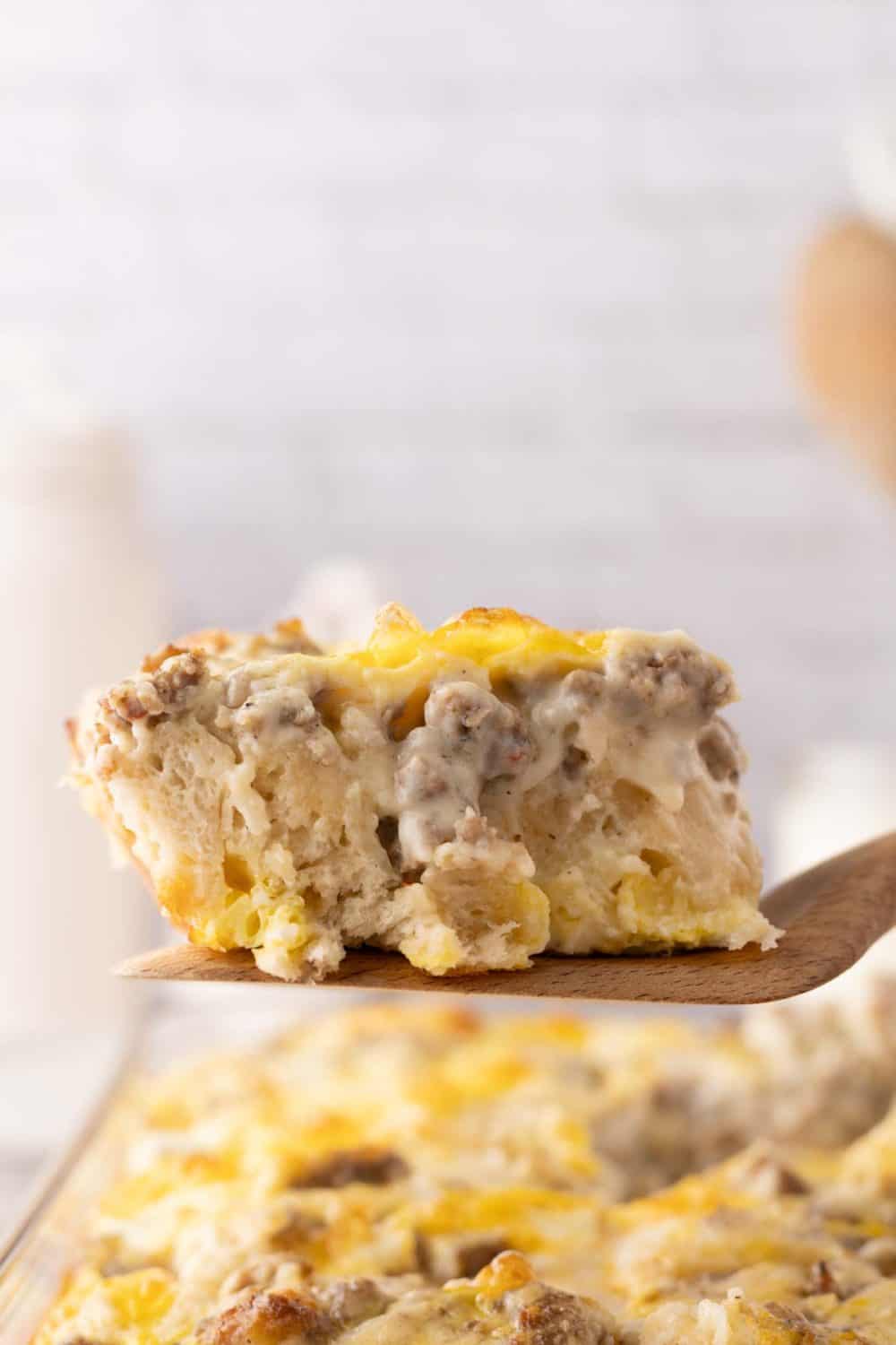biscuits and gravy casserole recipe in a 9x12 dish with a square serving on a wooden spatula.