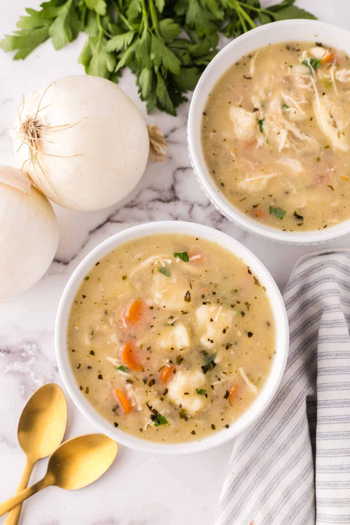 bisquick dumplings recipe in white bowls with golden spoons and onions to the side.