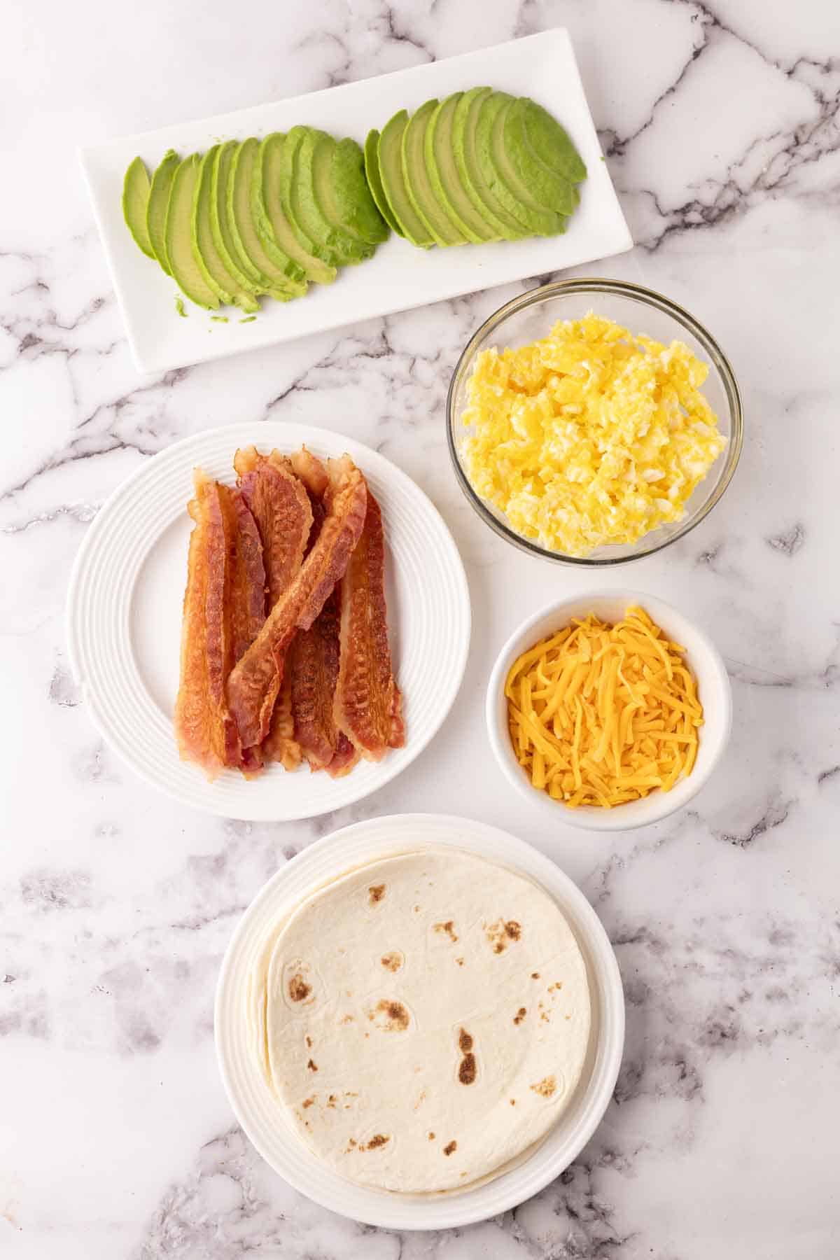 Portion bowls each with raw ingredient to make breakfast burritos.