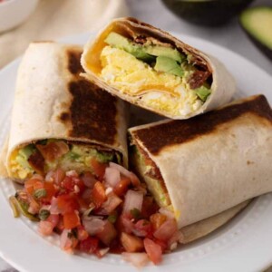 grilled and cut in half stack of breakfast burritos on a white plate with salsa and avocado.