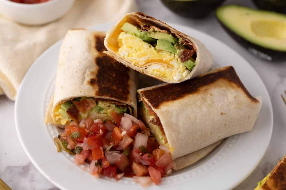 Grilled and cut in half stack of breakfast burritos on a white plate with salsa. 