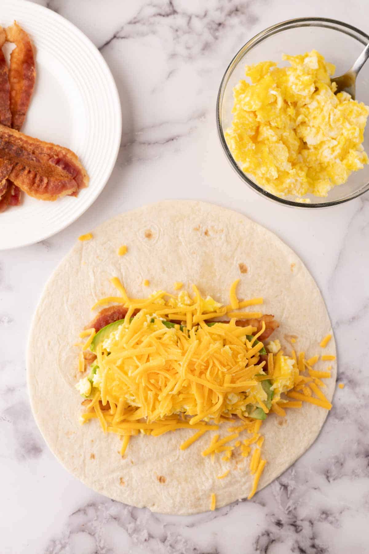 Flour tortilla with ingredients in progress to make breakfast burritos.