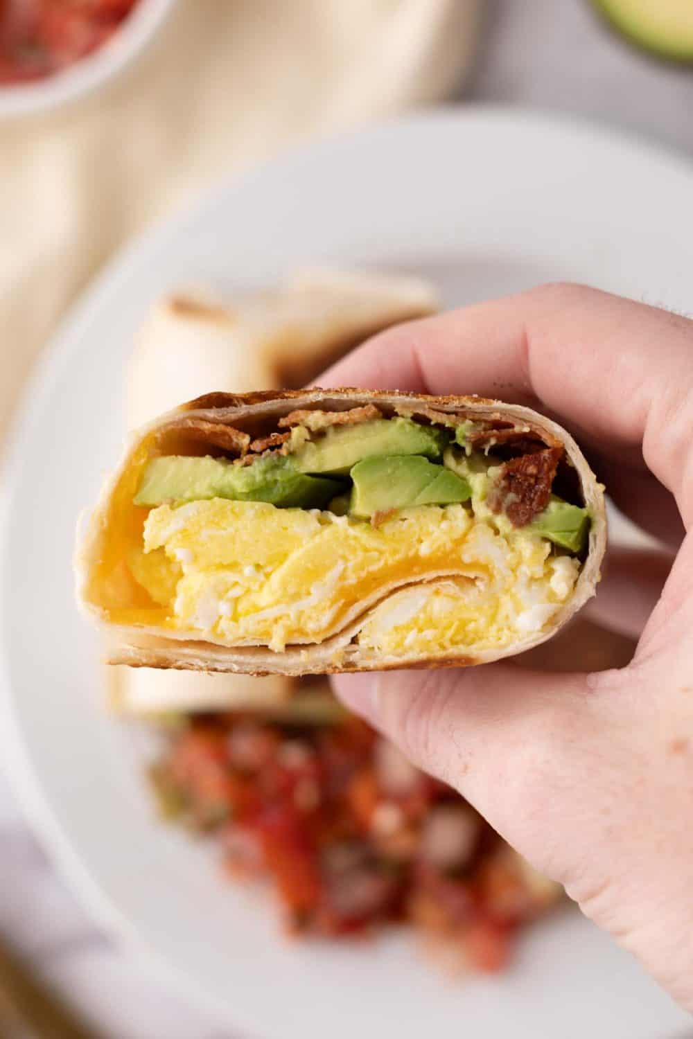 Hand holding a sliced breakfast burrito ready to eat.