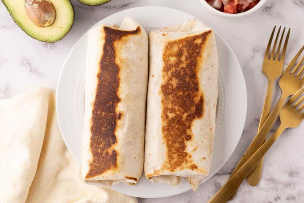 Grilled wrap around flour tortilla breakfast burritos with avocado and salsa to the side.